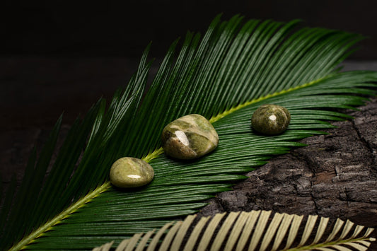 Three polished green stones rest on a large dark green palm leaf against a dark wooden surface.