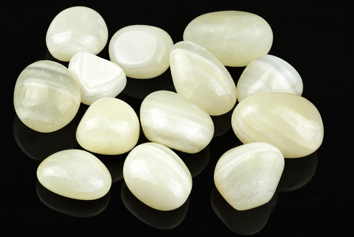 Twelve polished white and cream-coloured stones with subtle banding, arranged on a dark reflective surface.