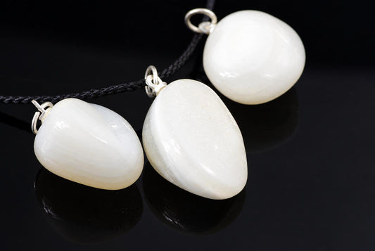Three white pebble-shaped pendants with silver-toned loops on dark cords, resting on a dark reflective surface.