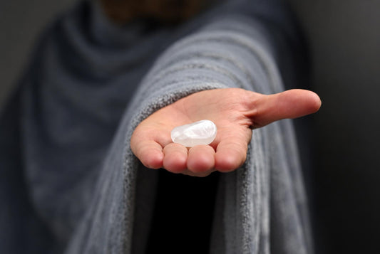 A person in a grey robe holds a smooth, white, translucent stone in their open palm against a dark background.