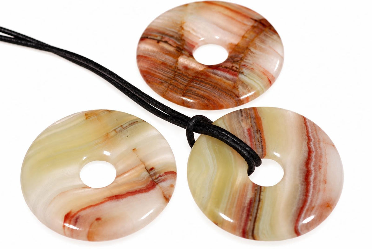 Three polished donut-shaped pendants with swirling cream, red and brown stripes on a white surface.