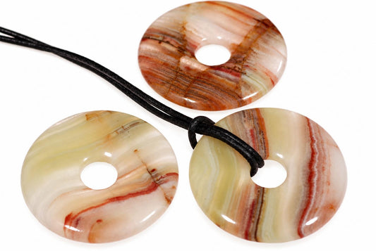 Three polished donut-shaped pendants with swirling cream, red and brown stripes on a white surface.