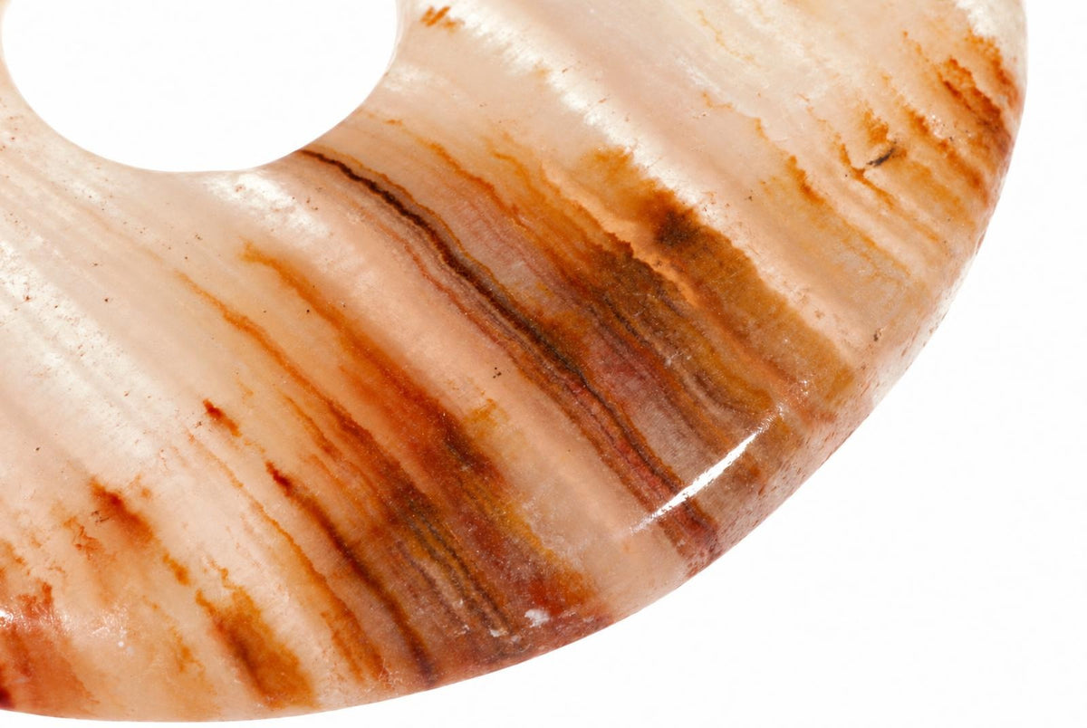 A polished, donut-shaped pendant with a smooth white surface and brownish-orange striped patterns on a plain background.