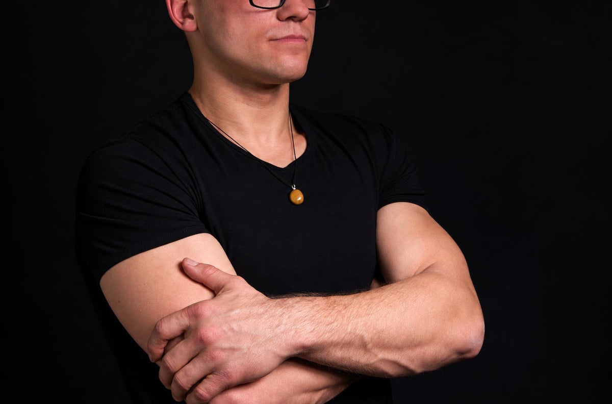 A man in a black t-shirt wears a yellow jasper pendant on a dark surface.