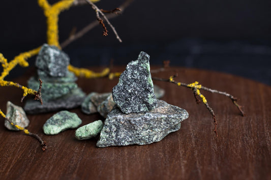 Several rough, green and grey speckled stones are arranged on a dark wooden surface with yellow lichen-covered branches.